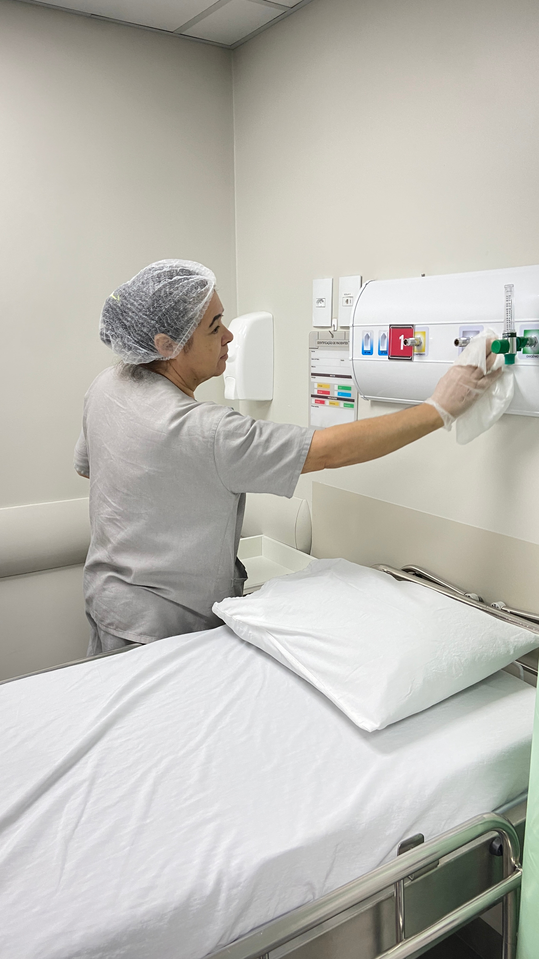 Profissional SLG higienizando painel de gases em quarto hospitalar