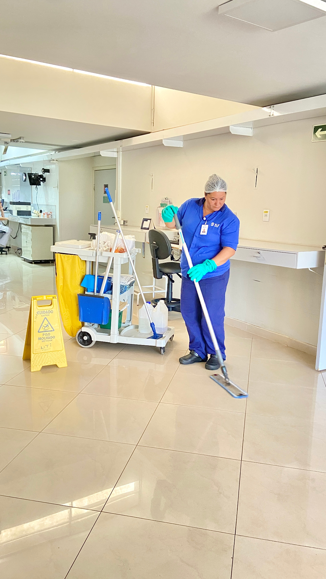 Colaboradora SLG realizando limpeza úmida de piso em corredor hospitalar
